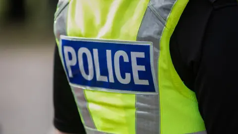 Getty Images A close up shot of the Police logo on the back of a high-vis stab jacket - the lettering is white, surrounded by a blue square - sitting on the high vis material of the vest no face or identifiable features can be seen