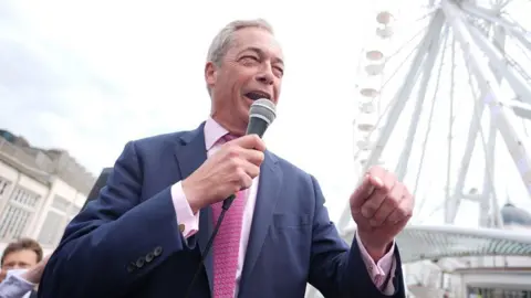 Getty Images Nigel Farage addresses crowds in Clacton, with microphone in hand and ferris wheel in the background