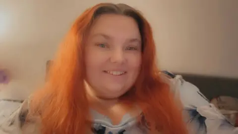 Lauren Barford-Dowling Lauren Barford-Dowling smiles at the camera. She has long, red hair and is wearing a flowery top and sitting on a dark sofa.