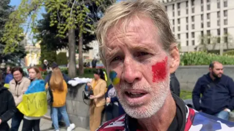 AFPTV/AFP via Getty Images This screengrab taken from AFPTV shows Ryan Wesley Routh at a protest supporting Ukraine in April 2022.  Routh is wearing an American flag shirt and has face paint in the colours of the Ukrainian flag on his cheek.