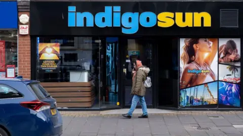 Getty Images A lady walking along the street in front of a shop bearing the name Indigo Sun