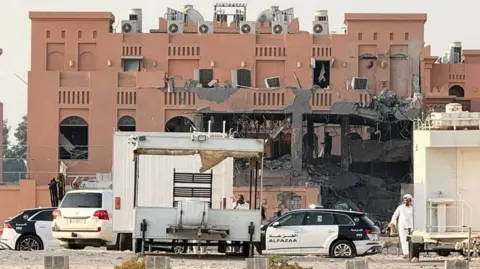 Reuters A part of a red building is damaged - hollowed out and destroyed - after a strike. Police vehicles are parked in front. 
